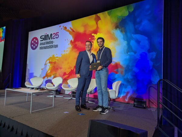 Award presentation at the SIIM Annual Meeting with two men on stage, one receiving a recognition plaque, colorful background, and event branding, emphasizing medical imaging and informatics.