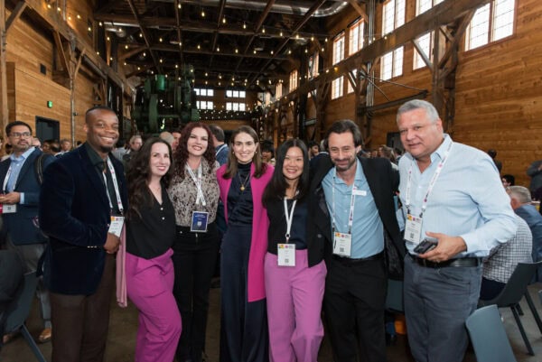 Diverse group of professionals attending the SIIM Annual Meeting in a spacious, rustic conference hall with wooden walls, high ceilings, and warm lighting, engaging in networking and industry insights.