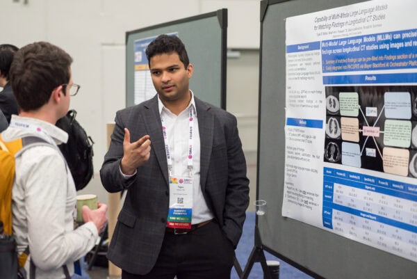Deep in discussion at the SIIM Annual Meeting, showcasing a scientific poster on multi-modal large language models for longitudinal CT studies, highlighting AI in medical imaging.