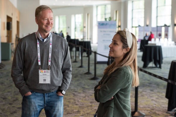 Brightly lit conference lobby during the SIIM Annual Meeting, featuring two professionals engaging in conversation, with event banners and registration area in the background.