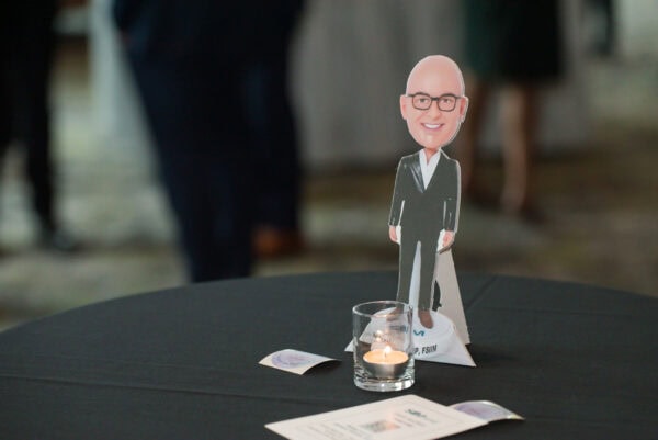 Funny caricature of a bald man with glasses dressed in a black suit standing on a table at the SIIM Annual Meeting.
