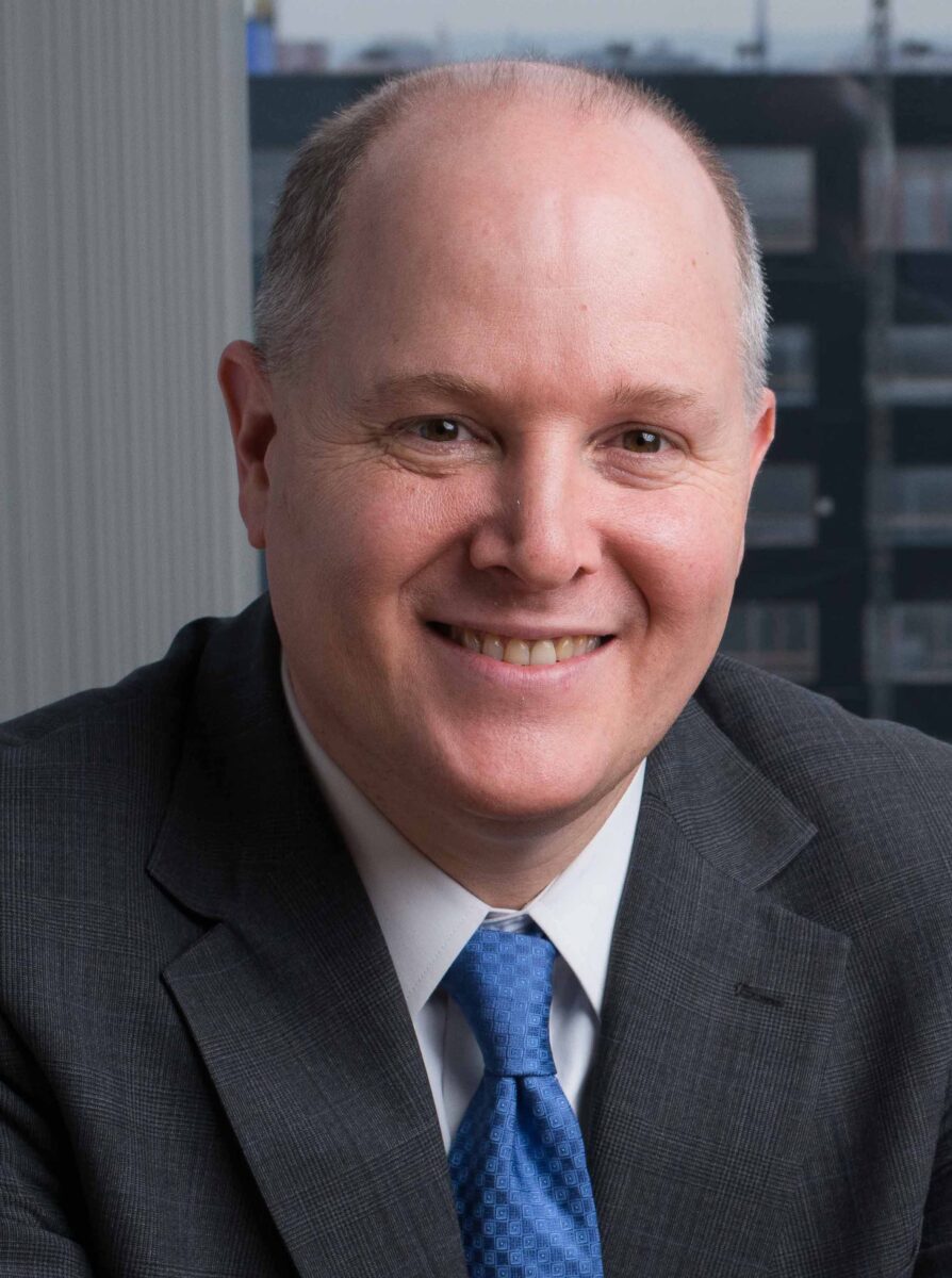 A professional headshot of a smiling man in a business suit at the SIIM Annual Meeting, emphasizing healthcare imaging and medical informatics.