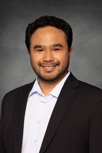 Professional portrait of Theo Dapamede, MD, PhD, attending the SIIM Annual Meeting, showcasing a healthcare expert in a formal suit.