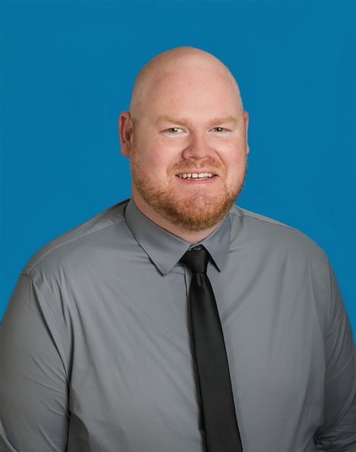 Portrait of Mark Jones at the SIIM Annual Meeting, showcasing a professional individual in a gray shirt and black tie against a blue background.