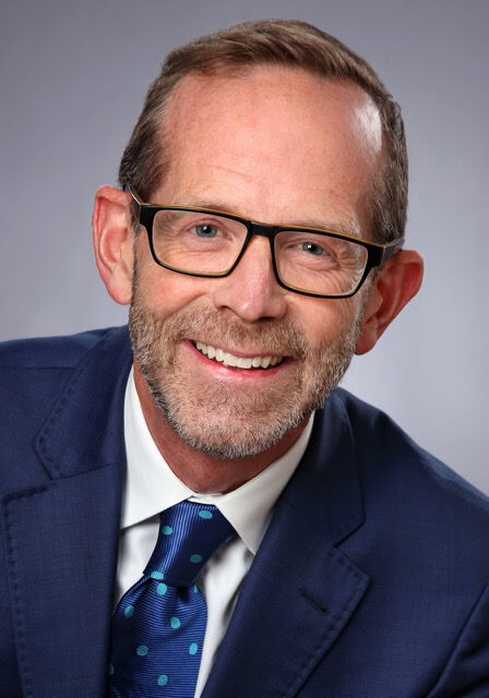 An image of a smiling professional man wearing glasses, a navy suit, and a blue tie, attending the SIIM Annual Meeting, a leading event in medical imaging and informatics.