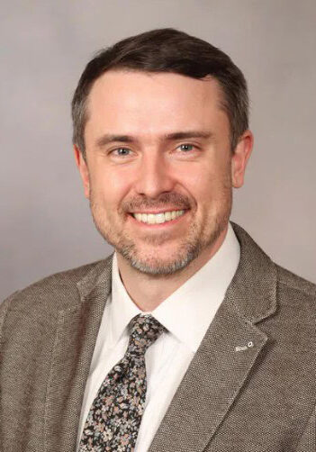 A professional headshot of a smiling man in business attire, suitable for the SIIM Annual Meeting, emphasizing networking and medical imaging expertise.