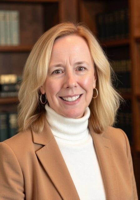 Jeanne Nauman smiling at the SIIM Annual Meeting, standing in front of a bookshelf with medical books, wearing a tan blazer and white turtleneck.